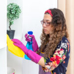 happy woman rubber gloves wiping white shelves with yellow rag using cleaning spray home light living room